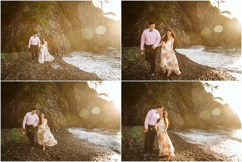 Snohomish & seattle wedding photographer | gsquared weddings photography a couple walks along a rocky beach at sunset during their deception pass engagement session in june 2020 holding hands and smiling as sunlight creates a warm glow and lens flare with waves crashing against a cliff in the background | wedding photo by gsquared weddings