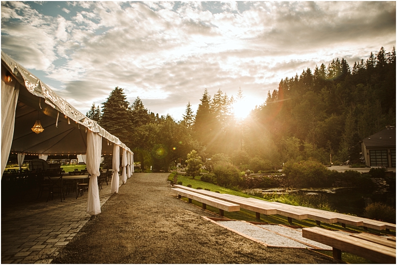 Snohomish & seattle wedding photographer | gsquared weddings photography a sunlit outdoor event space at gray bridge features a white draped tent on the left wooden benches on the right and lush trees in the background under a partly cloudy sky at sunset | wedding photo by gsquared weddings