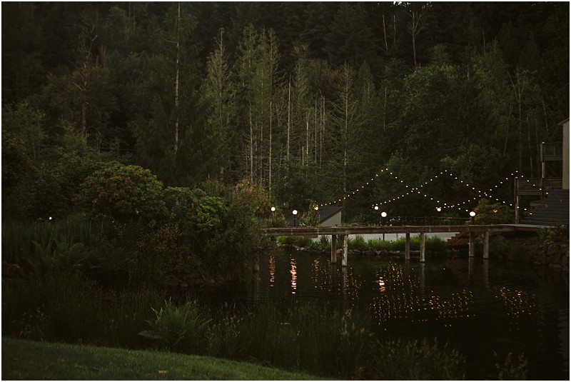 Snohomish & seattle wedding photographer | gsquared weddings photography a gray bridge over a pond is decorated with string lights and lanterns surrounded by dense trees and greenery creating a serene and festive atmosphere at dusk | wedding photo by gsquared weddings
