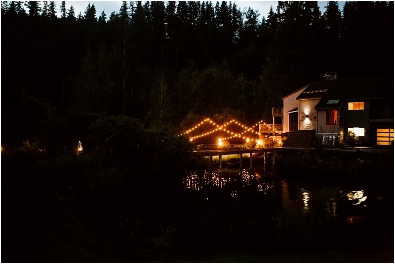 Snohomish & seattle wedding photographer | gsquared weddings photography a house by a pond at night with string lights illuminating a gray bridge and reflecting on the water surrounded by tall trees in the background | wedding photo by gsquared weddings
