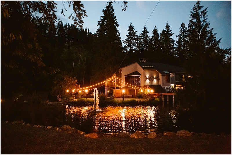 Snohomish & seattle wedding photographer | gsquared weddings photography a cozy house by a pond at dusk surrounded by tall trees and a gray bridge is lit by glowing string lights and a fountain in the water creating a warm and inviting atmosphere | wedding photo by gsquared weddings