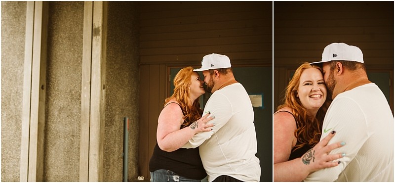 Snohomish & seattle wedding photographer | gsquared weddings photography two people stand close together laughing and embracing in front of a plain building wall The woman with long red hair smiles at the camera while her partner in a white cap faces hercapturing a joyful gray bridge engagement moment | wedding photo by gsquared weddings