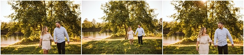 Snohomish & seattle wedding photographer | gsquared weddings photography a couple walks hand in hand on grass by a river at pemberton farm smiling at each other with trees and sunlight in the background during their snohomish engagement session | wedding photo by gsquared weddings