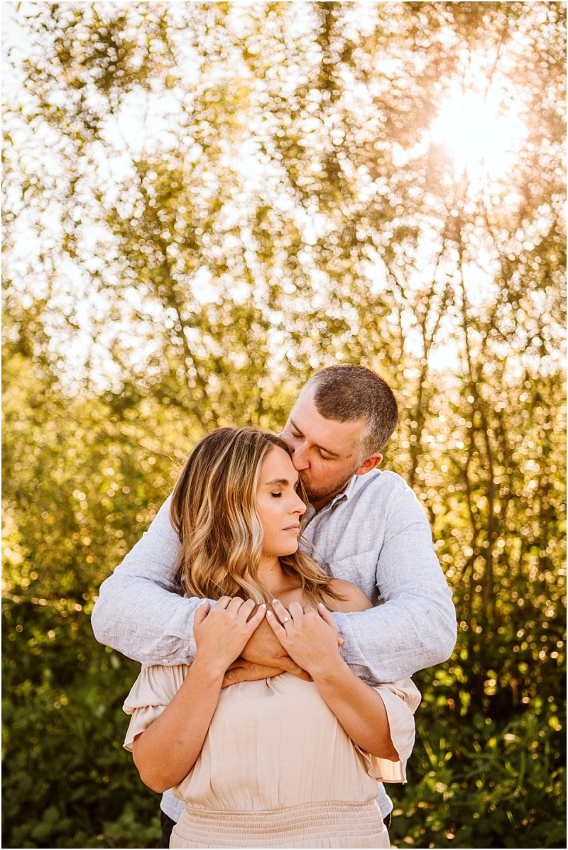 Snohomish & seattle wedding photographer | gsquared weddings photography a couple embraces outdoors at pemberton farm with the man gently hugging and kissing the womans head They stand in front of leafy trees bathed in warm golden light during their snohomish engagement session | wedding photo by gsquared weddings