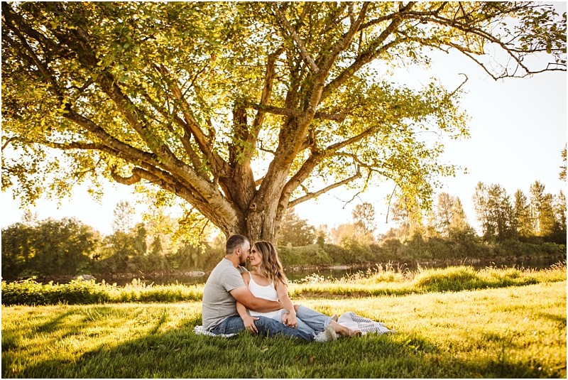 Snohomish & seattle wedding photographer | gsquared weddings photography a couple sits closely together on a blanket under a large tree in a sunlit park at pemberton farm engagement snohomish gazing at each other lovingly The green grass and warm sunlight filtering through the branches create a peaceful scene | wedding photo by gsquared weddings