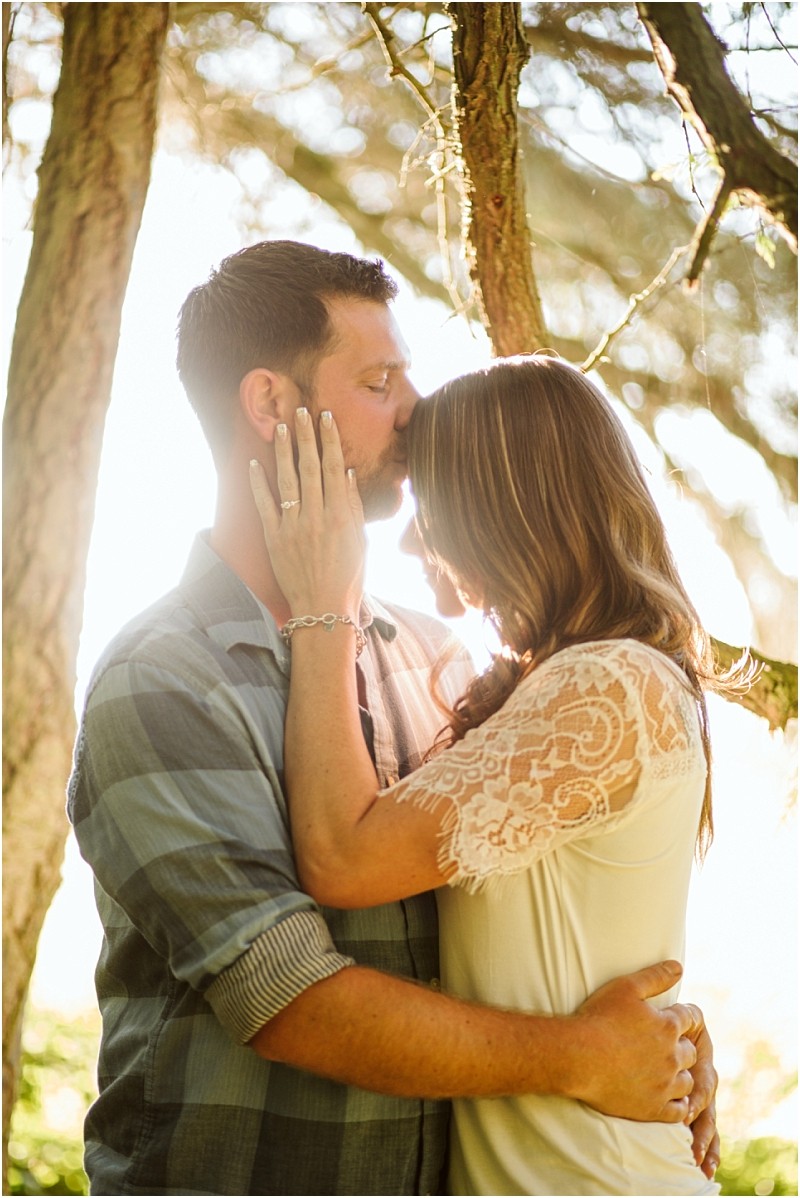 Snohomish & seattle wedding photographer | gsquared weddings photography a man gently kisses the forehead of a woman while holding her close in a sunlit forest at deception pass she touches his face as golden august light streams through the trees behind them | wedding photo by gsquared weddings