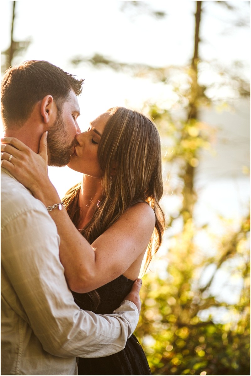 Snohomish & seattle wedding photographer | gsquared weddings photography a couple shares a kiss outdoors at deception pass surrounded by sunlight and trees The woman holds the mans face gently and both appear affectionate and happy during their august engagement in the natural setting | wedding photo by gsquared weddings
