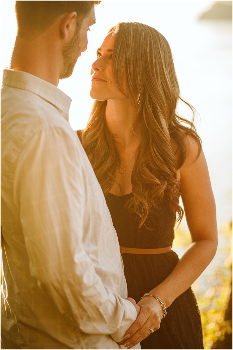 Snohomish & seattle wedding photographer | gsquared weddings photography a woman with long wavy hair gazes lovingly at a man while holding his hands outdoors in warm golden sunlight during their deception pass august engagement Both appear happy and relaxed sharing an intimate moment together | wedding photo by gsquared weddings