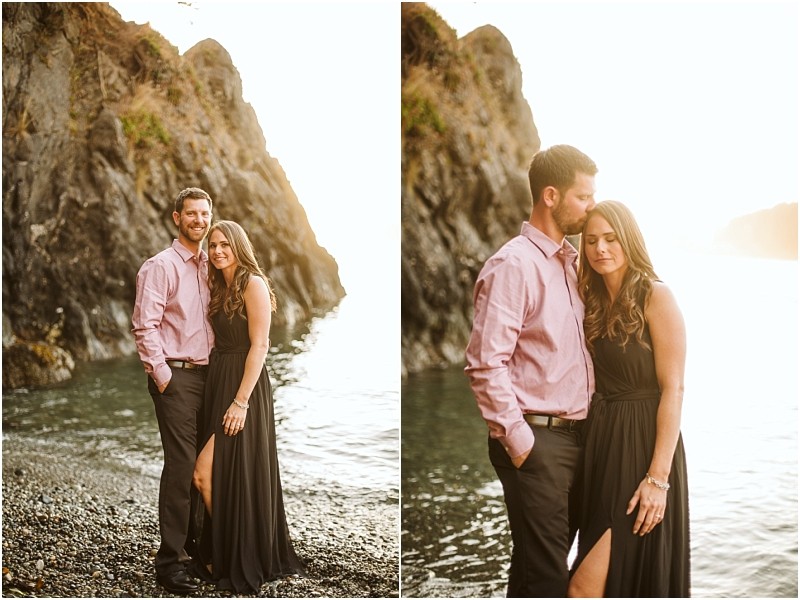 Snohomish & seattle wedding photographer | gsquared weddings photography a couple stands close on a rocky beach at sunset during their deception pass august engagement The man wears a pink shirt and dark pants the woman is in a sleeveless black dress looking affectionate by the water and cliffs | wedding photo by gsquared weddings