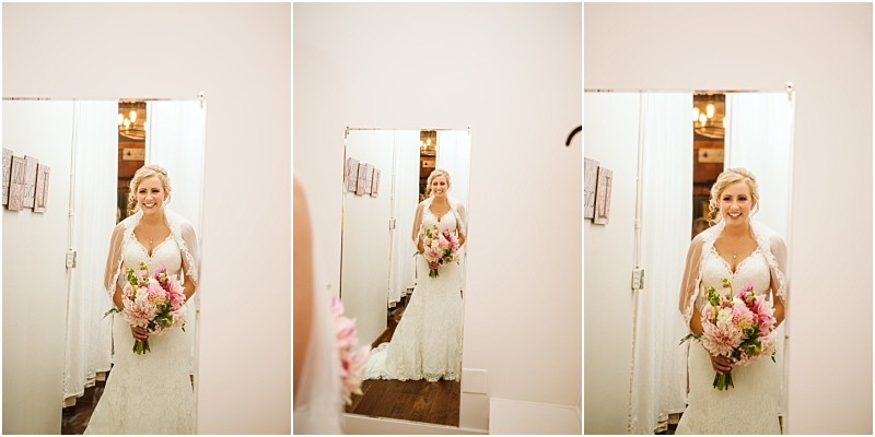 Snohomish & seattle wedding photographer | gsquared weddings photography a bride in a white lace gown and veil holds a bouquet of pink flowers smiling as she admires her reflection before her a summer barn at holly farm wedding in a softly lit room with white walls | wedding photo by gsquared weddings