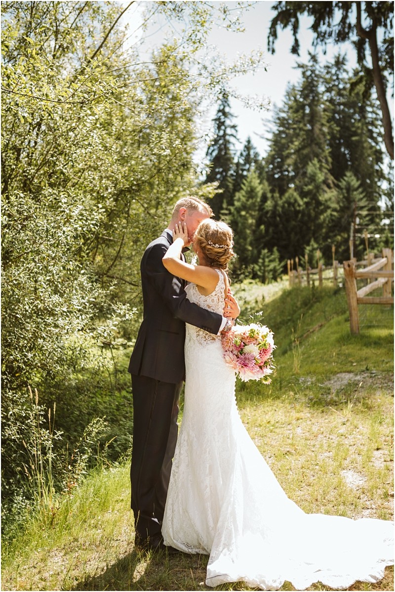 A bride and groom embrace and kiss outdoors on a sunny day in snohomish surrounded by lush greenery and trees The bride holds a bouquet of pink flowers while both shine in their formal wedding attire Snohomish wedding photography
