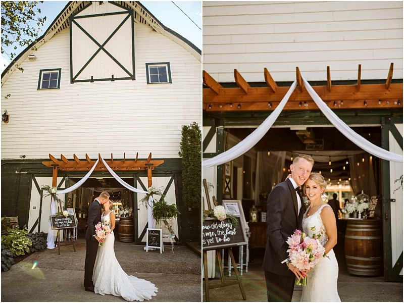 A bride and groom stand smiling in front of a white snohomish barn decorated with drapes and flowers posing for wedding photos The barn door is open revealing string lights and rustic decorations inside Snohomish wedding photography