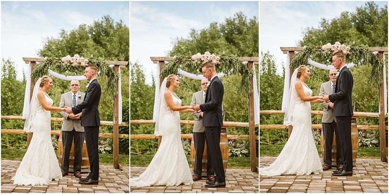A bride and groom stand under a floral arch holding hands during an outdoor snohomish wedding ceremony with an officiant behind them The scene is bright and surrounded by lush greenery Snohomish wedding photography