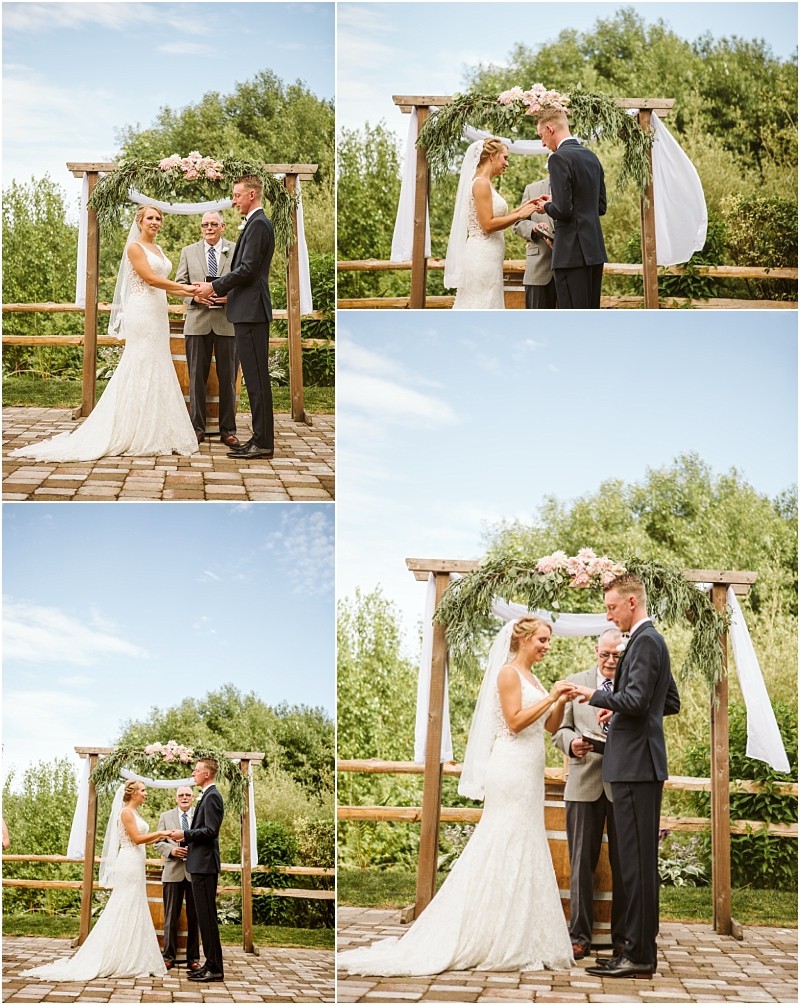 A bride and groom exchange vows outdoors under a wooden arch with white drapes and pink flowers accompanied by an officiant during a sunny snohomish wedding ceremony Snohomish wedding photography