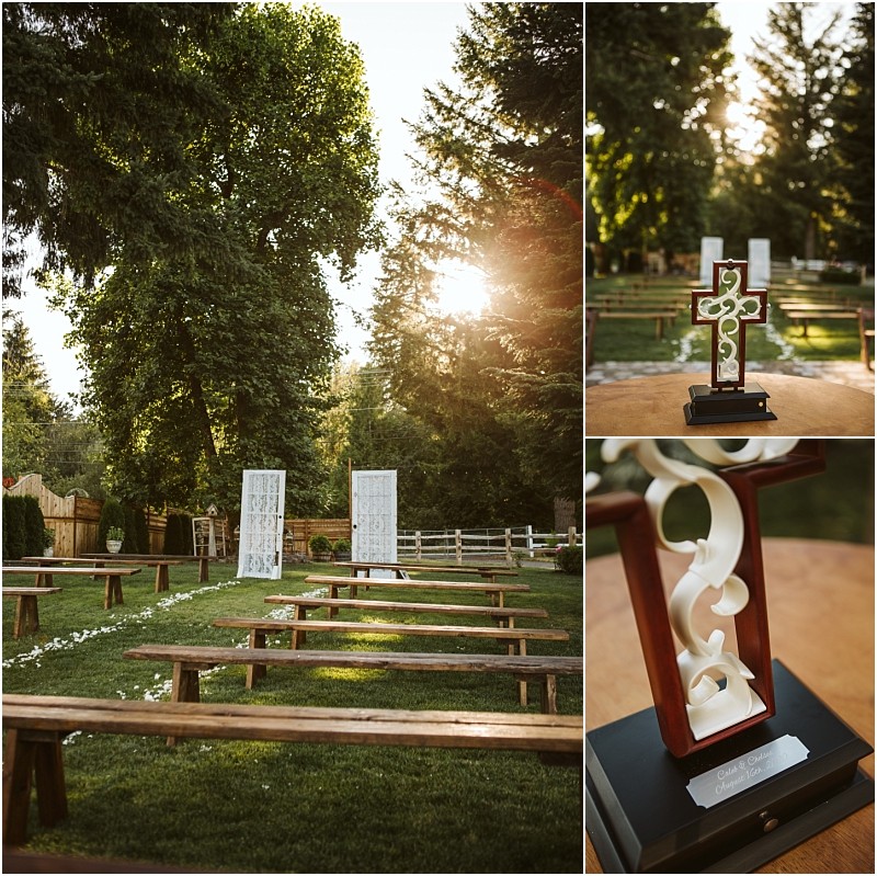 Outdoor wedding setup in snohomish with wooden benches on grass white lace panels at the altar and a decorative cross on a stand Sunlight filters through tall green trees surrounding the peaceful setting Snohomish wedding photography