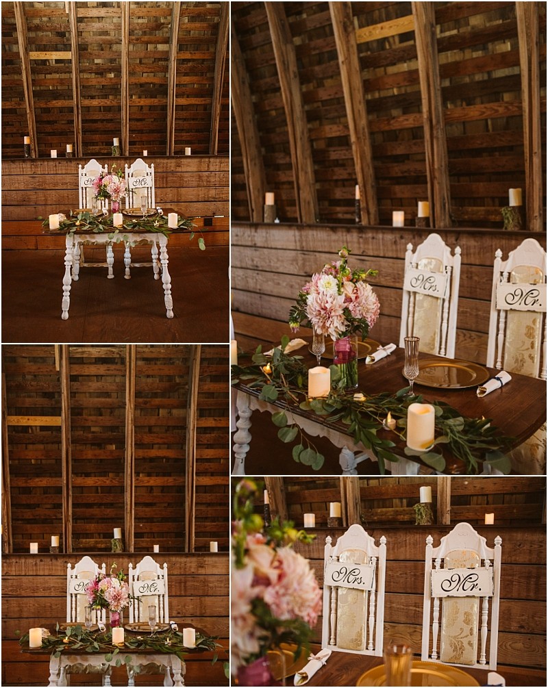 A rustic sweetheart table setup in a snohomish wooden barn decorated with candles greenery gold plates floral arrangements and two white chairs labeled mr  and mrs  Snohomish wedding photography