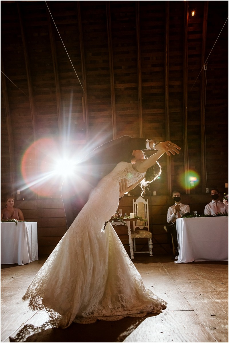 A bride and groom share a dramatic dip during their first dance in a rustic snohomish barn backlit by bright lighting with guests seated at tables in the background Snohomish wedding photography