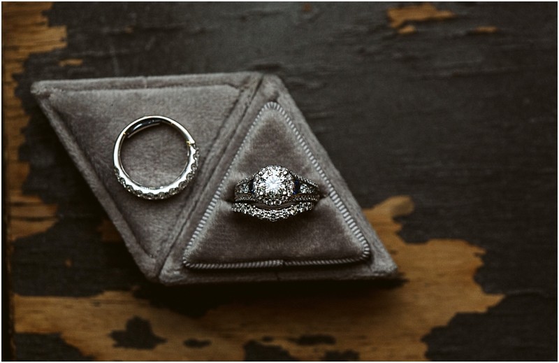 A close up of two diamond ringsone band and one with a large central diamonddisplayed on a gray triangular velvet ring box atop a dark distressed wooden surface in snohomish Snohomish wedding photography