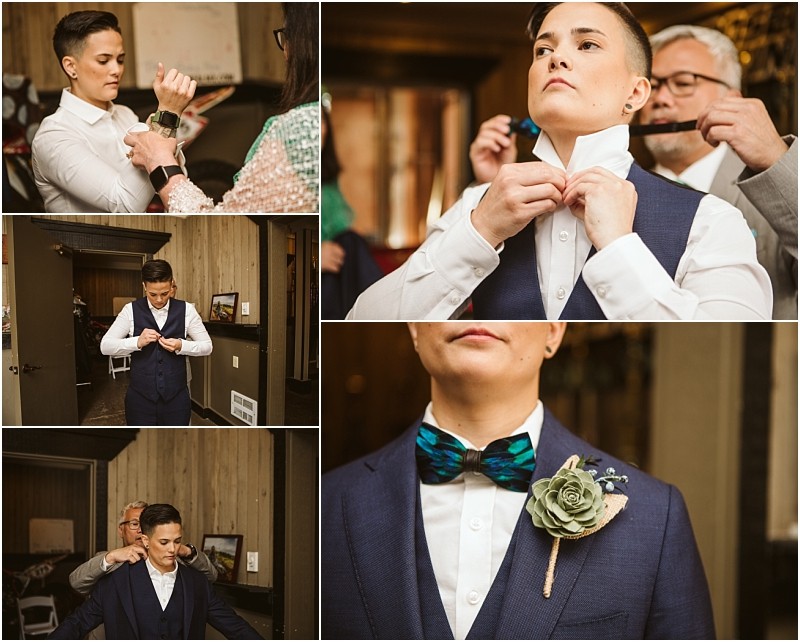 A person in a navy suit gets ready for a formal event in snohomish adjusting their collar and bow tie as a boutonniere is pinned on by others in a warmly lit room Snohomish wedding photography