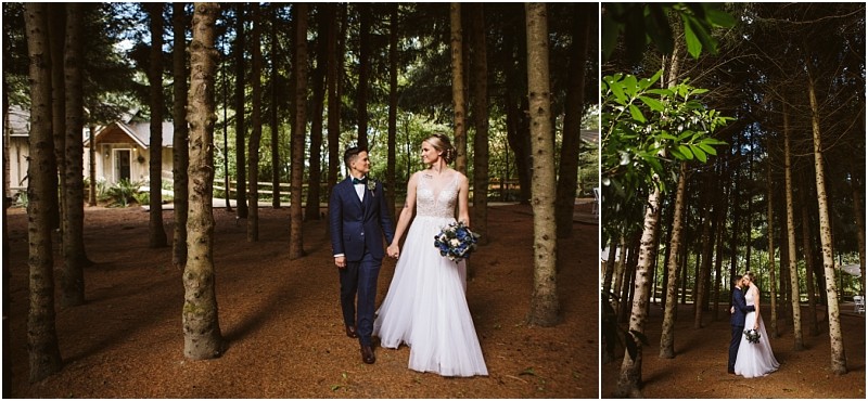 A bride and groom stand together in a forested snohomish area holding hands and smiling at each other The bride wears a white gown and holds a bouquet of flowers the groom wears a navy suit Sunlight filters through the trees Snohomish wedding photography