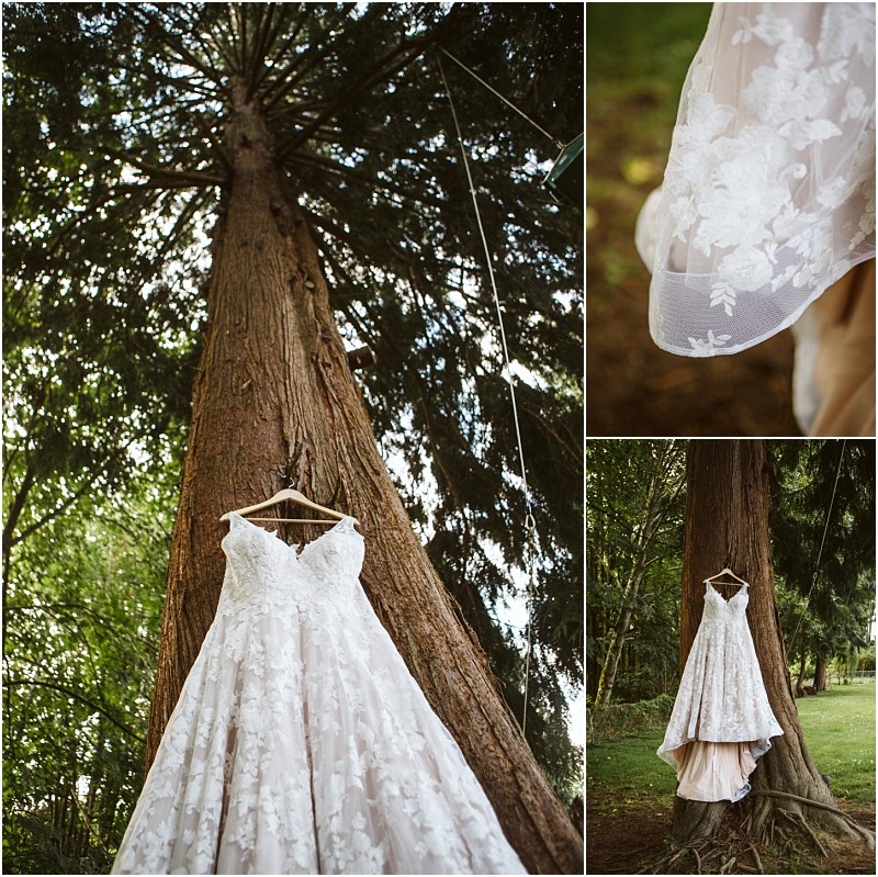 A white lace wedding dress with floral patterns hangs from a tree in a lush green snohomish outdoor setting Close up and full length shots highlight the dress details and nature backdrop Snohomish wedding photography