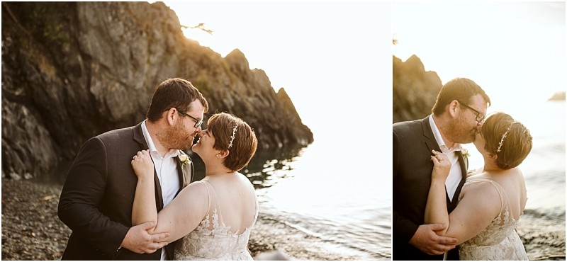 A newlywed couple in formal attire shares a joyful kiss on a rocky snohomish beach at sunset with sunlight reflecting on the water behind them Snohomish wedding photography