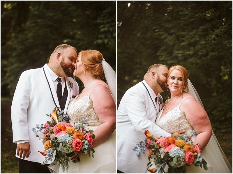 A newlywed couple poses outdoors in snohomish in their wedding attire The groom wears a white tuxedo and kisses the bride who holds a colorful bouquet and wears a white dress with a veil in front of a lush green background Snohomish wedding photography