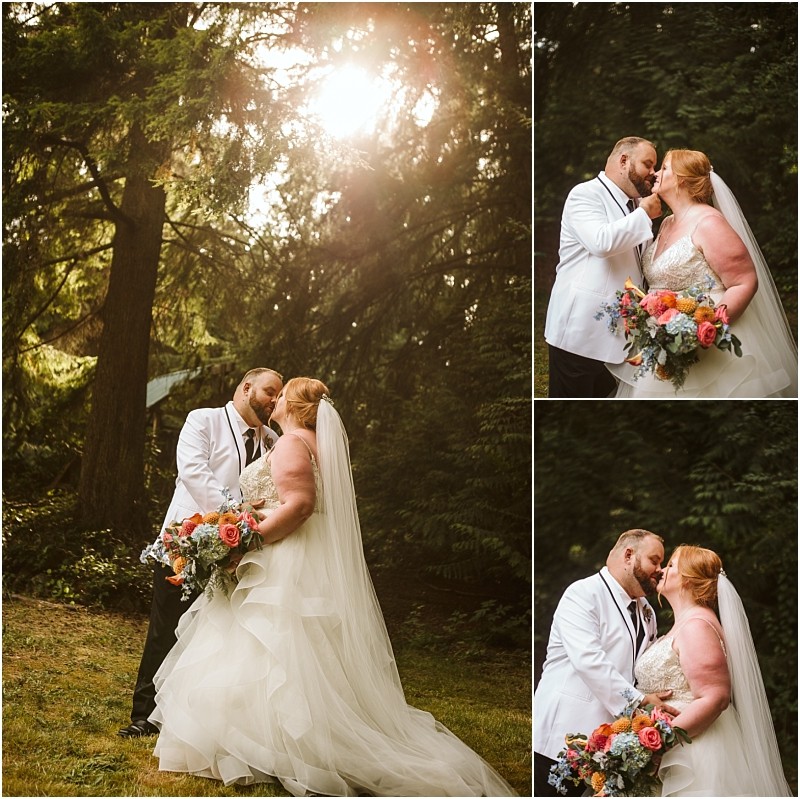 A bride and groom stand close together in a sunlit snohomish forest embracing and kissing The bride wears a white gown and veil holding a colorful bouquet the groom wears a white jacket and black pants Snohomish wedding photography