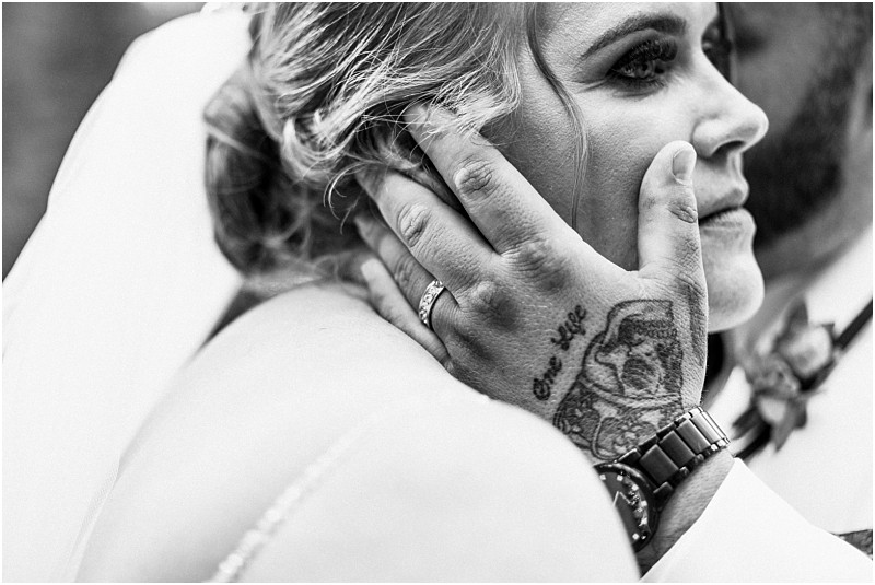 A black and white close up of a snohomish bride and groom embracing The grooms tattooed hand gently holds the brides face displaying a wedding band The bride looks emotional her eyes gazing off to the side Snohomish wedding photography