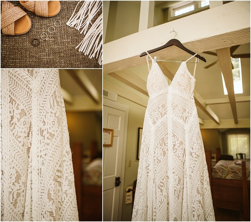 A lacy white wedding dress hangs on a wooden hanger in a sunlit snohomish room Nearby tan sandals fringe accessories and wedding rings are arranged neatly on a brown textured surface Snohomish wedding photography