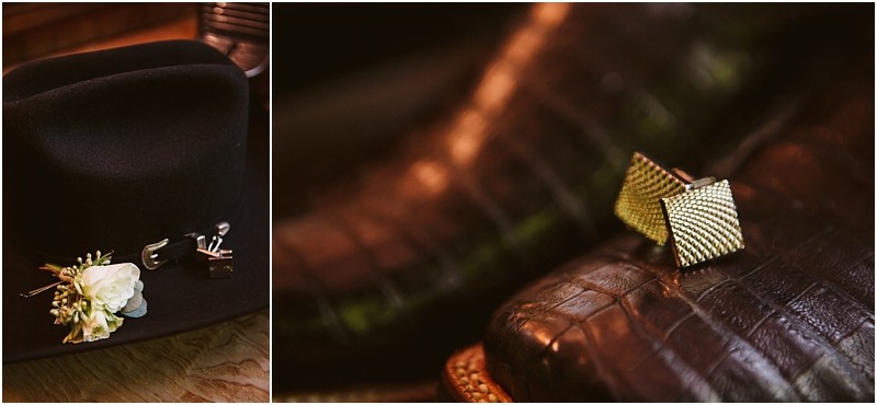 A black hat with a small white flower and silver pin on the brim sits beside textured gold cufflinks all elegantly arranged on a dark crocodile patterned leather surface in snohomish Snohomish wedding photography