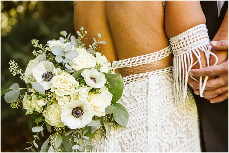 A bride in a lace dress holds a bouquet of white flowers and greenery while standing next to her partner in formalwear their hands gently linkeda romantic moment captured at a charming snohomish wedding The image focuses on the bouquet and dress details Snohomish wedding photography