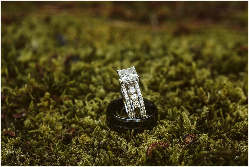 A diamond engagement ring and a wedding band with smaller diamonds are placed upright on a bed of green moss outdoors in snohomish Snohomish wedding photography