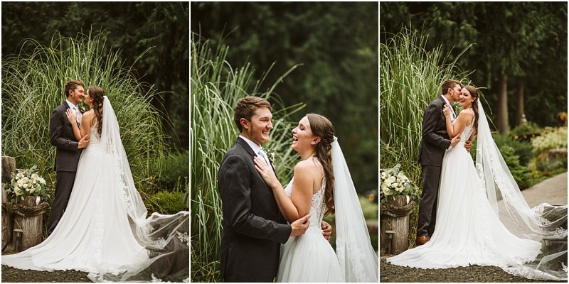 A bride and groom stand outdoors in front of tall green grasses in snohomish embracing and smiling at each other in wedding attire The bride wears a long white dress with a veil and the groom wears a dark suit Snohomish wedding photography