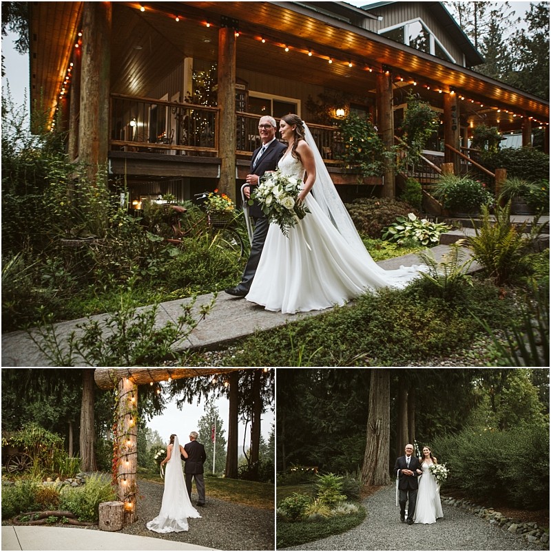 A bride in a white gown and veil walks with an older man outside a rustic snohomish building decorated with string lights surrounded by lush greenery and tall trees Snohomish wedding photography