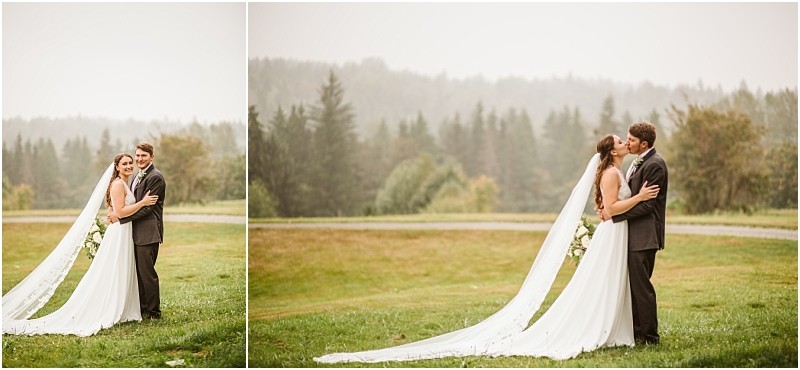 A bride and groom stand outdoors on a grassy snohomish field with trees in the background The bride wears a long white dress with a flowing veil and the groom is in a suit They embrace and share a kiss looking happy and in love Snohomish wedding photography