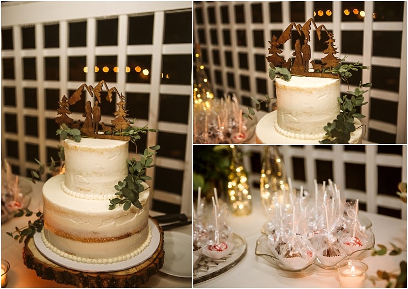 A two tiered white cake with a mountain and tree topper sits on a wood slice decorated with greenerya charming snohomish touch Nearby individually wrapped treats and candles are arranged on a table with a grid patterned backdrop Snohomish wedding photography