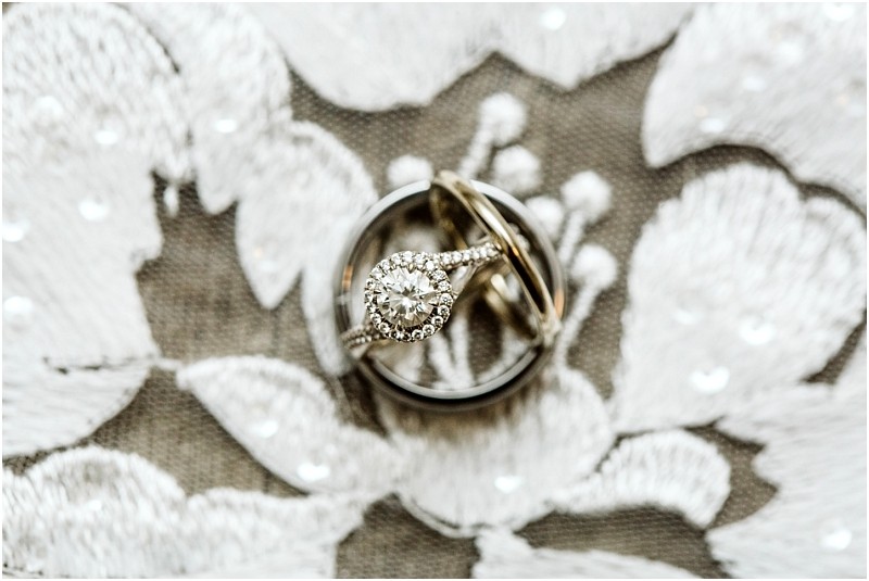 A diamond engagement ring and a wedding band are displayed together on white embroidered lace fabric The rings are arranged artistically highlighting the sparkling diamond and intricate metalworka timeless snohomish romance captured perfectly Snohomish wedding photography