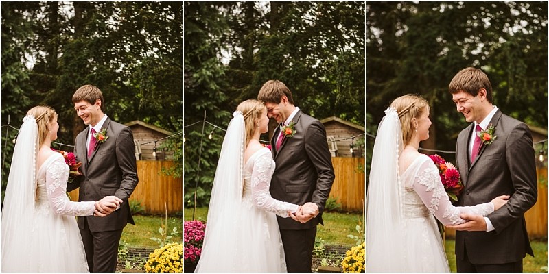 A bride and groom stand outside in snohomish holding hands and smiling at each other The bride wears a white dress with a veil the groom a suit with a burgundy tie They are surrounded by lush greenery and yellow flowers Snohomish wedding photography