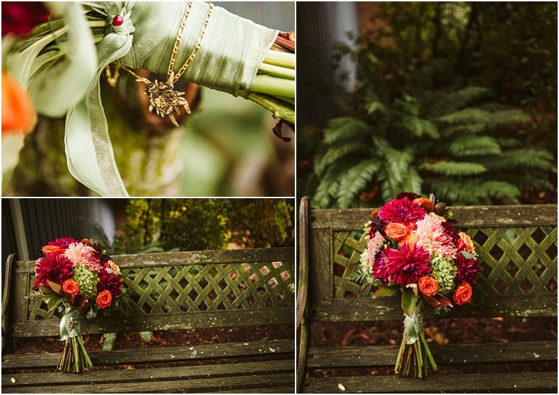 A bridal bouquet with red pink and orange flowers rests on a wooden bench outdoors in snohomish A close up reveals a green ribbon and a gold locket with a photo tied around the stems with green foliage in the background Snohomish wedding photography