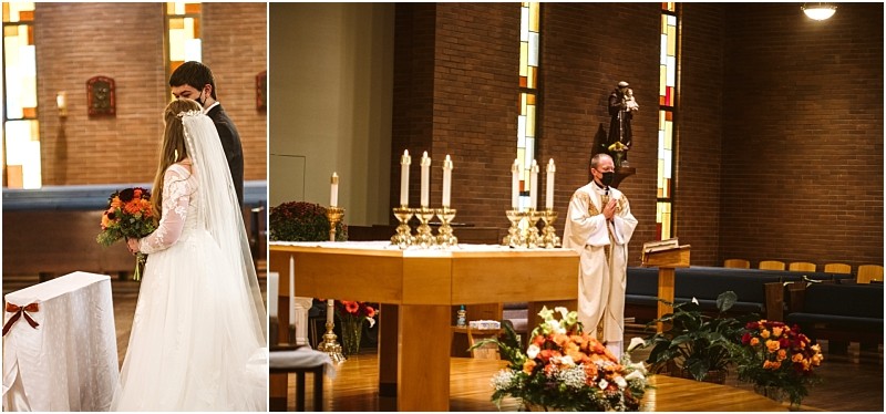 A bride and groom stand together at the altar while a mask wearing priest leads a wedding ceremony in a snohomish church decorated with autumn flowers and candles Snohomish wedding photography