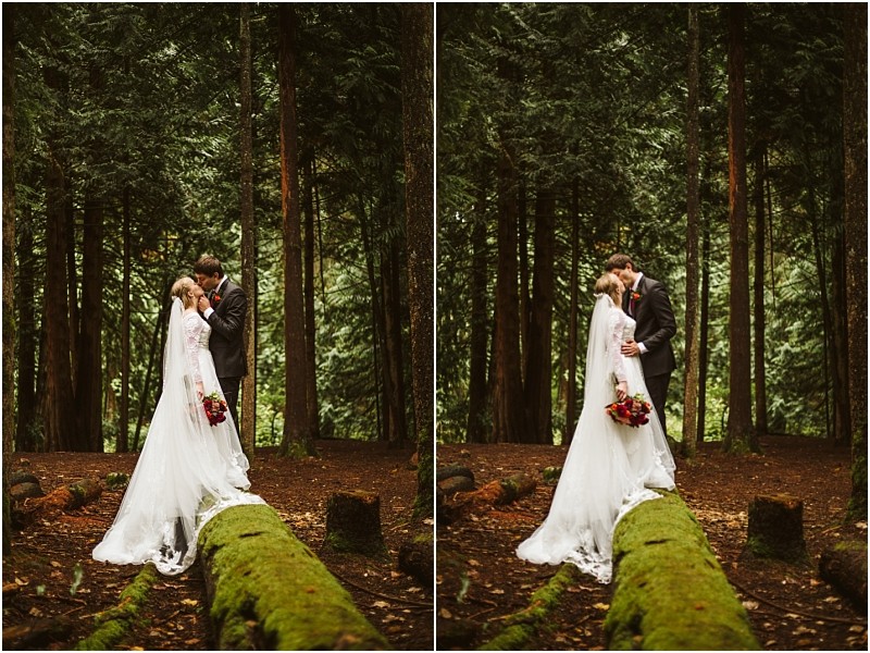 A bride and groom share a romantic moment in a snohomish forest standing on a moss covered log The bride wears a white gown and holds a bouquet of red flowers the groom is in a dark suit Sunlight filters through the tall trees Snohomish wedding photography