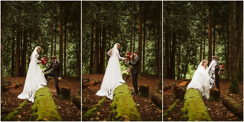 A bride in a white dress and a groom in a suit help each other balance as they walk along a mossy log in a snohomish forest surrounded by tall trees and lush greenery Snohomish wedding photography