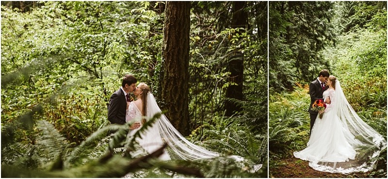 A bride and groom stand close together in a lush snohomish forest surrounded by green ferns and trees The bride wears a long white dress with a veil and the groom is in a dark suit as they share an intimate moment among the greenery Snohomish wedding photography