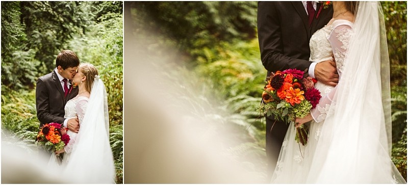 A bride and groom embrace in a lush green outdoor snohomish setting The bride holds a bouquet of red and orange flowers and wears a long veil while the groom is in a dark suit Both look lovingly at each other Snohomish wedding photography