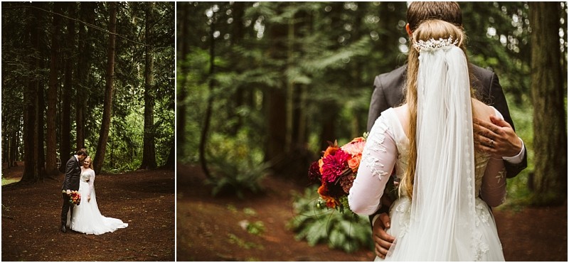 A bride and groom embrace in a forest near snohomish The bride wears a white dress with a long veil and holds a bouquet of red and orange flowers Tall trees surround them creating a natural serene backdrop for their special moment Snohomish wedding photography