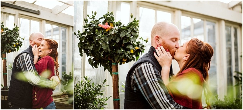 A couple stands in a sunlit snohomish greenhouse embracing and laughing The woman with red hair in a braid kisses the mans cheek as he smiles Potted plants and flowers surround them creating a joyful and romantic atmosphere Snohomish wedding photography