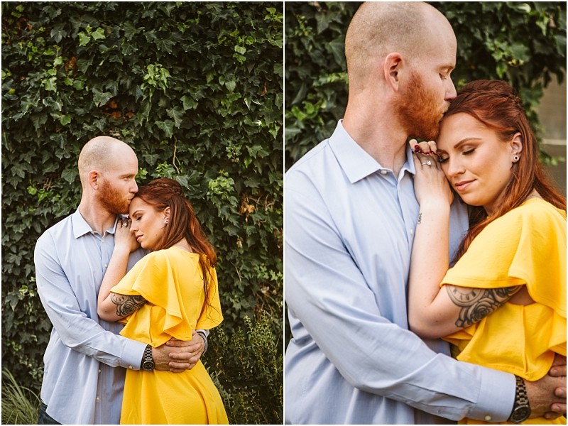 A couple stands close together outdoors in front of leafy greenery in snohomish The man with a beard and light blue shirt gently embraces the woman in a yellow dress as she rests her head on his chest with her eyes closed Snohomish wedding photography