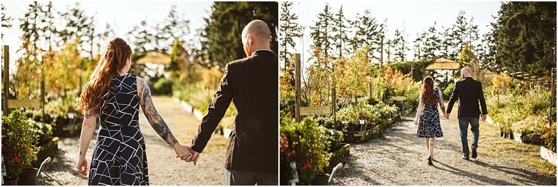 A couple holding hands walks down a sunlit path in a snohomish plant nursery surrounded by potted greenery and trees with sunlight streaming through the foliage in the background Snohomish wedding photography