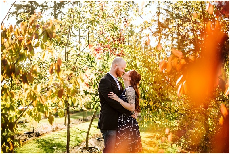 A couple stands in a sunlit snohomish garden facing each other and embracing with smiles Autumn colored leaves and trees surround them creating a warm romantic atmosphere Snohomish wedding photography